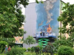sądecki artysta Mgr Mors (Mariusz Brodowski) z pomocnikiem malują mural "Kolej na Ciebie"