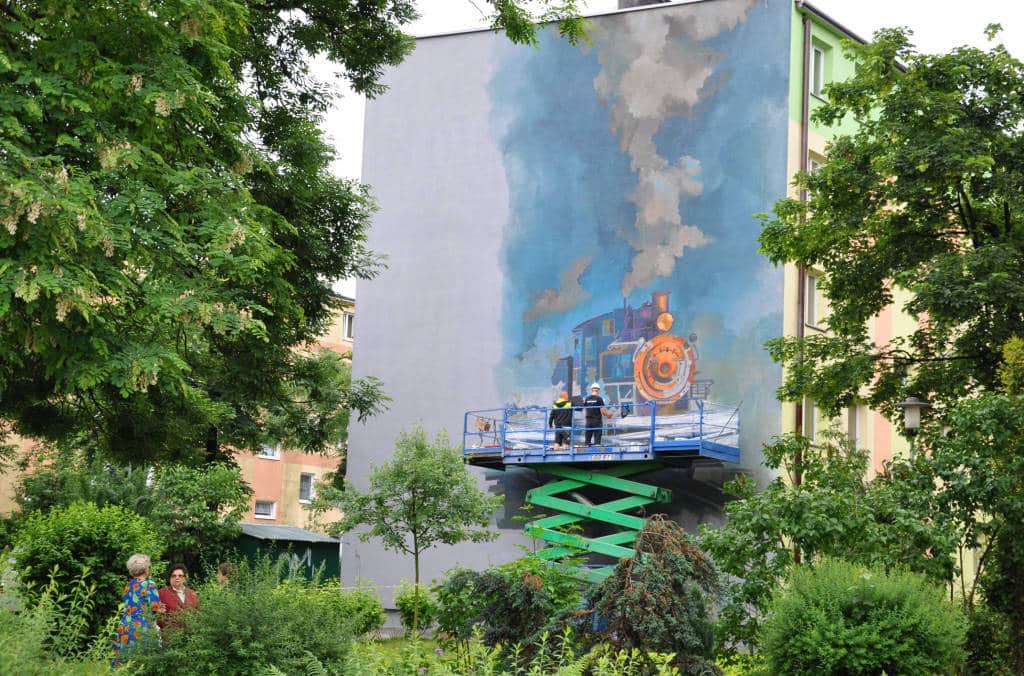 sądecki artysta Mgr Mors (Mariusz Brodowski) z pomocnikiem malują mural "Kolej na Ciebie"
