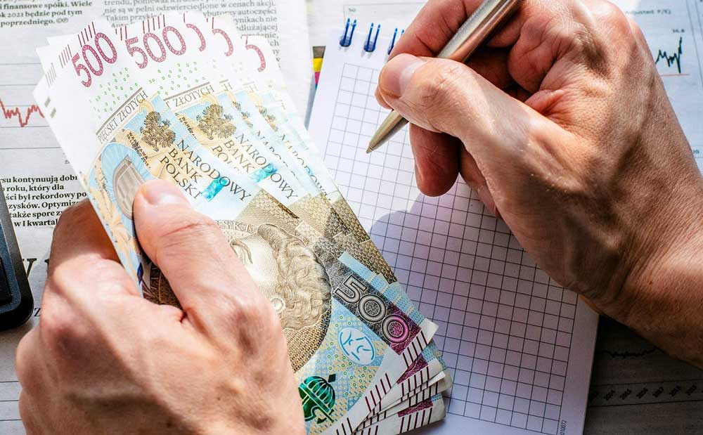 oszczędzamy na świętach. plik banknotów 500-złotowych w ręce, w drugiej ręce długopis