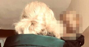 kobieta w zielonej kurtce i kamizelce z napisem Policja trzyma małego chłopca na rękach, stoją tłem, ich twarze są niewidoczne