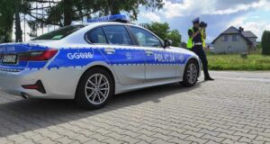 policjantka ruchu drogowego przy oznakowanym radiowozie, w dłoniach trzyma laserowy miernik prędkości