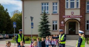 przejście dla pieszych pod szkołą, na nim dzieci i obok policjanci. Wygenerowane przez AI Google Imagen-4